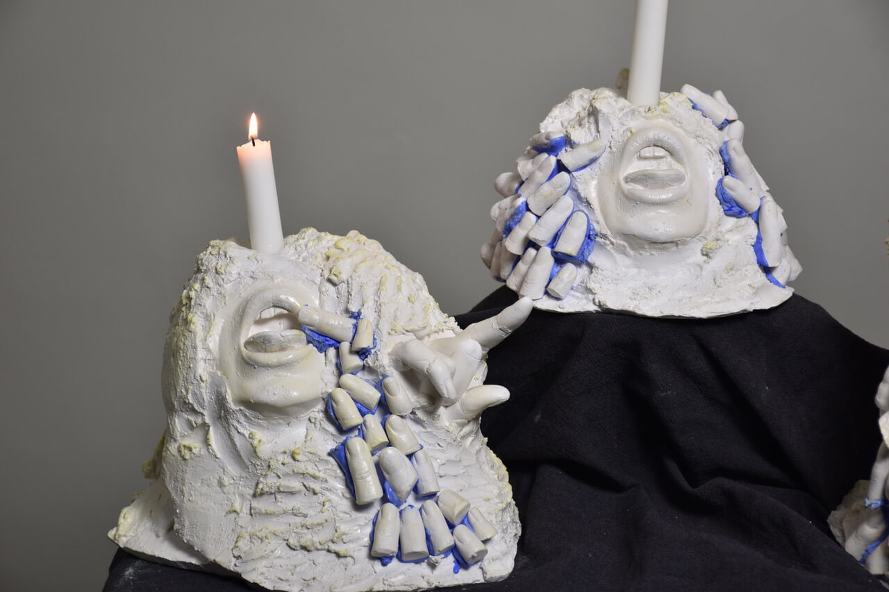 abstract candle holders with open mouths, hands and fingers on it